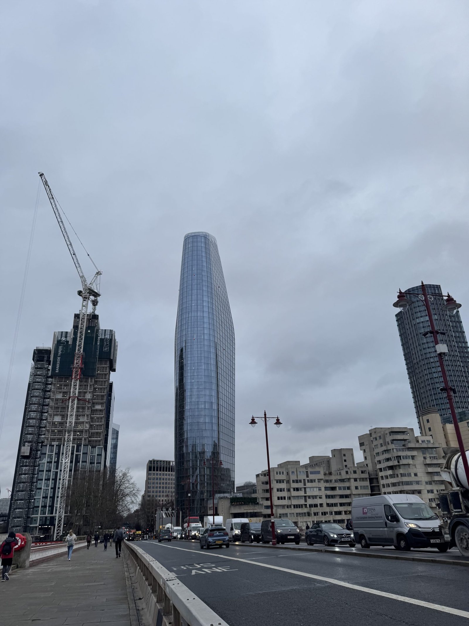 A city street with traffic and a tower block under construction behind a crane.