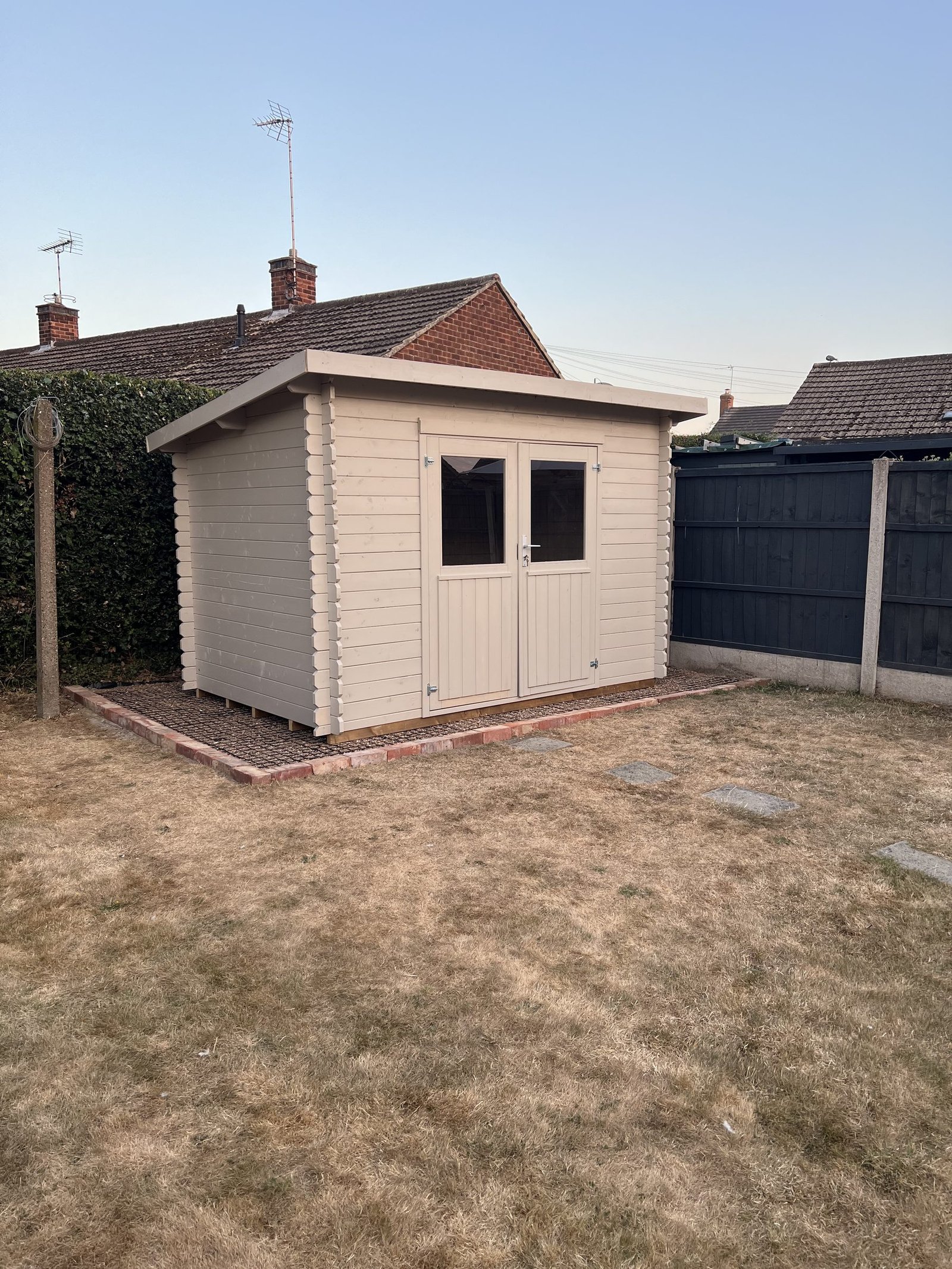 A finished garden building in a back garden on a clear day, photographed from an angle.