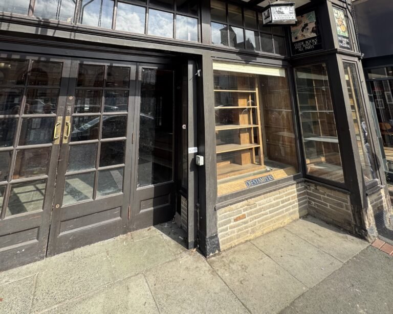 A traditional British timber shopfront with large glazed windows and a brick stall riser.