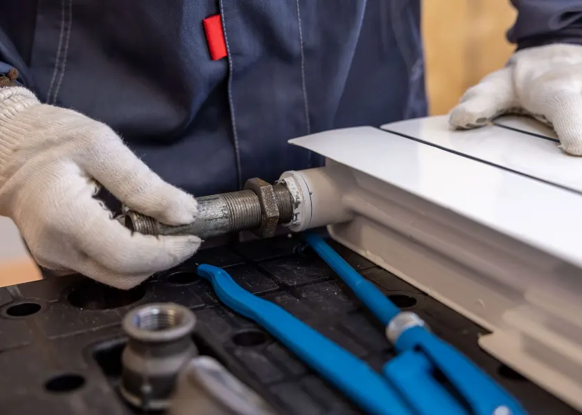 Gloved hands fitting a pipe to a radiator