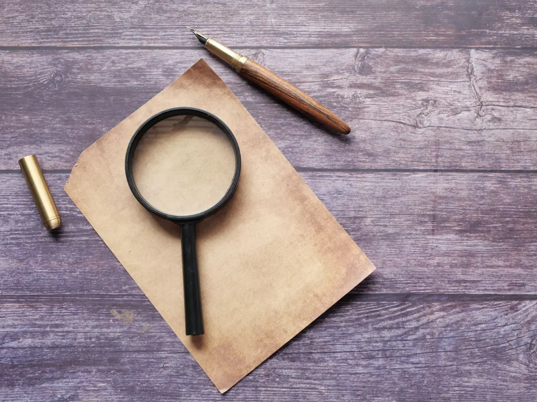 A magnifying glass on a sheet of paper next to a pen