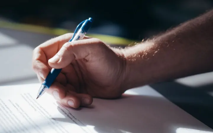 A hand writing on a document with a blue pen